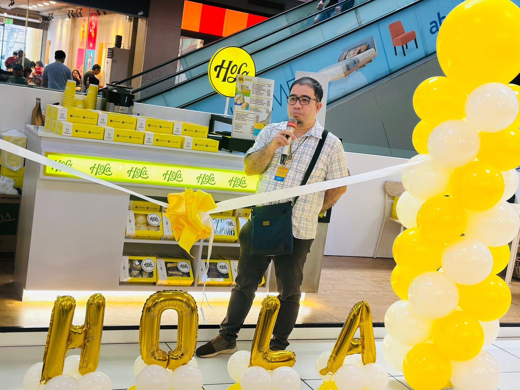 A Hola kiosk opening inside a shopping mall, with boxed breads on display and HOLA balloon letters
