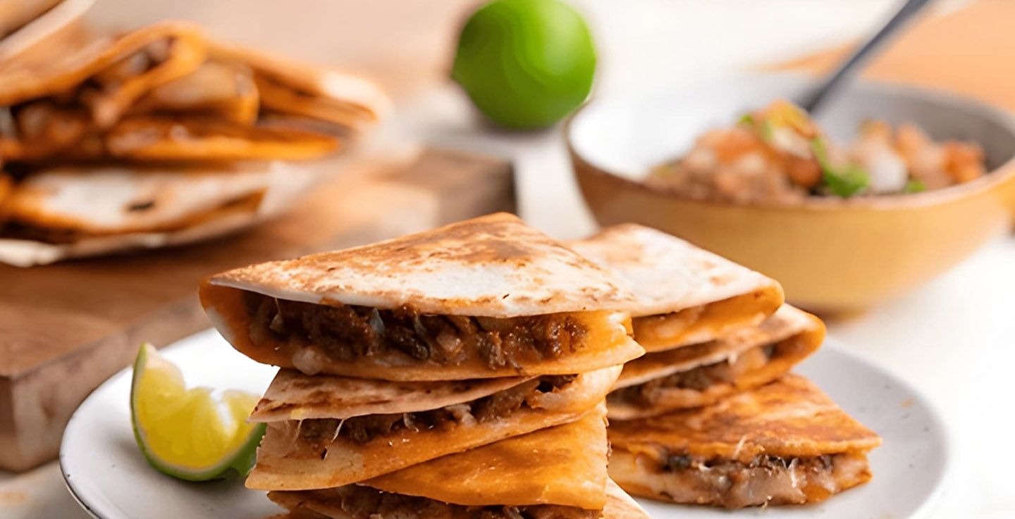 Hola Beef Quesadillas — grilled quesadilla wedges stuffed with seasoned beef and melted cheese, stacked on a plate with lime wedges