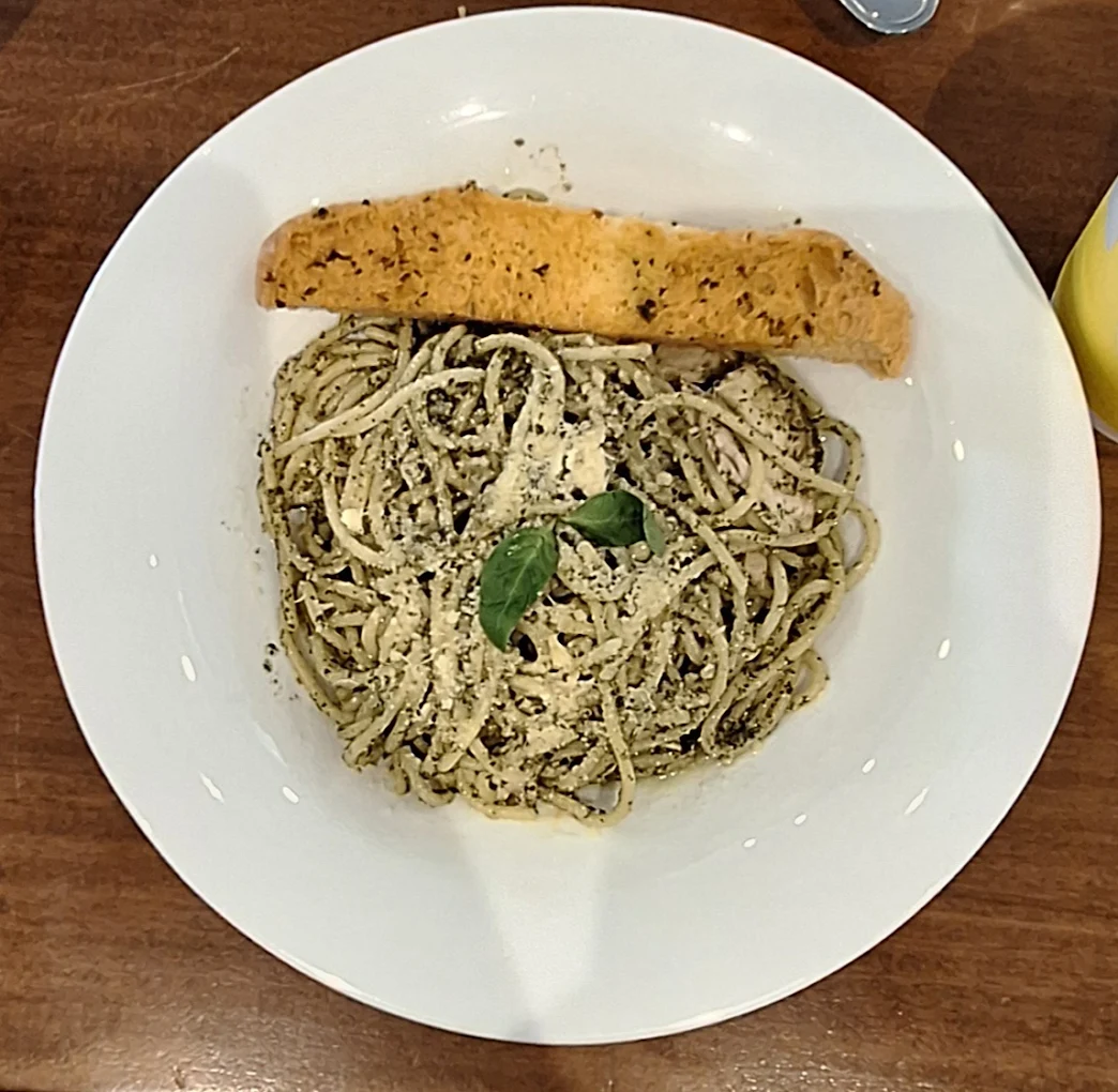 Hola Chicken Pesto — al dente spaghetti coated in vibrant basil pesto with shredded chicken, topped with fresh basil and parmesan, served with garlic bread